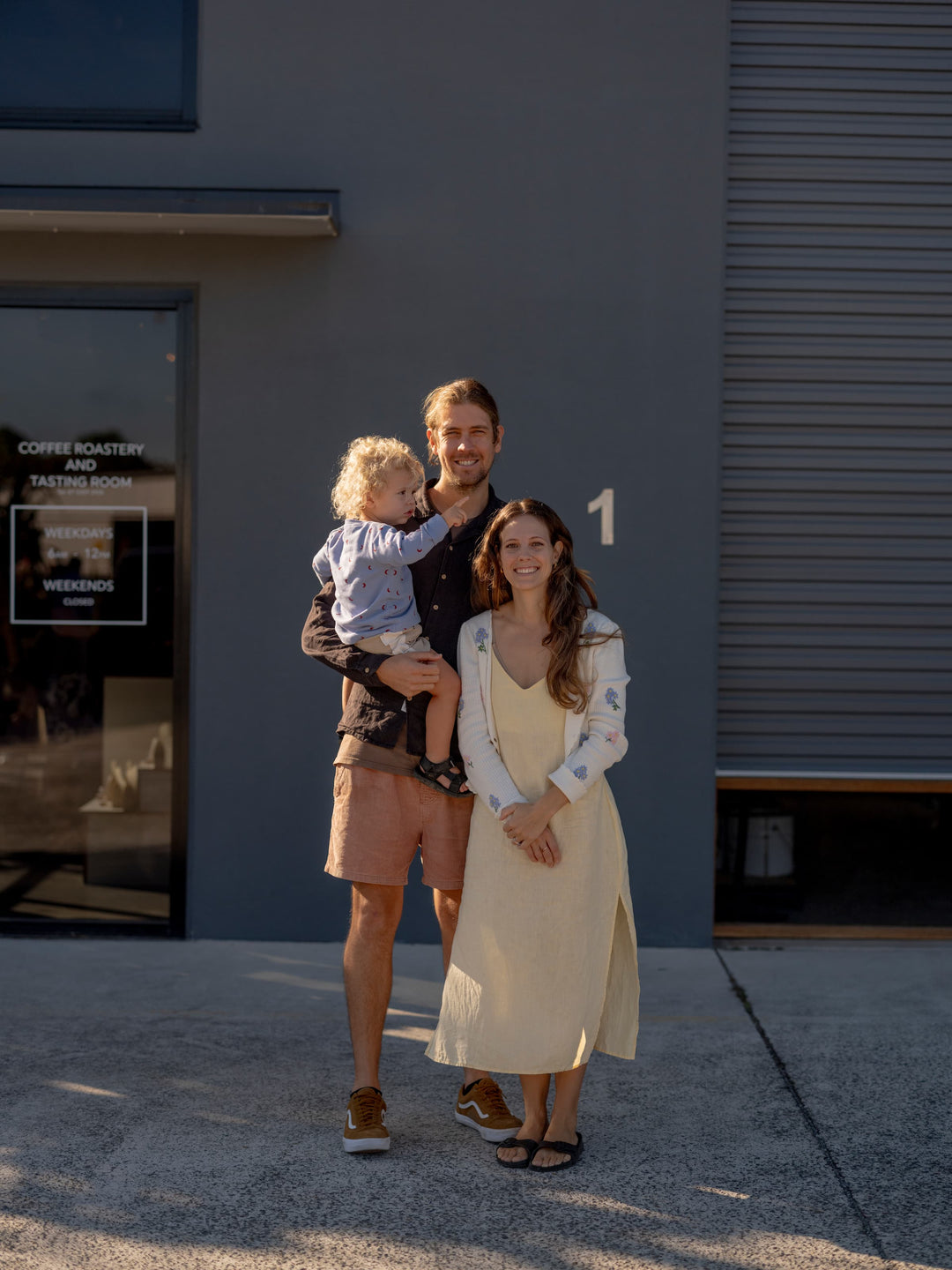 Family of three standing in front of a building with a sign.